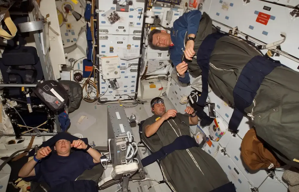 three astronauts sleeping in tethered sleeping bags on the iss