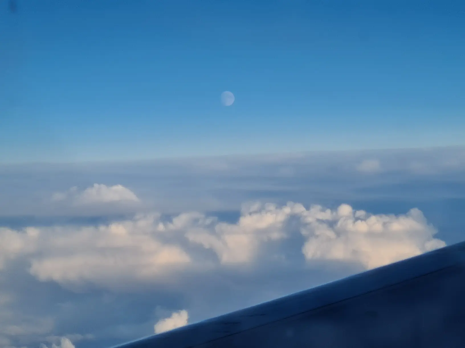 photo of the moon visible during daylight taken on plane